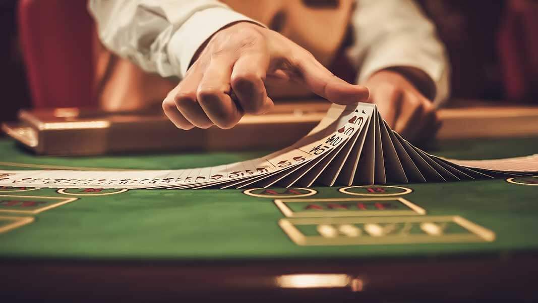 b1820696-b214-11e9-9705-3ebc7820c324 Blackjack dealer shifting deck of cards on casino table